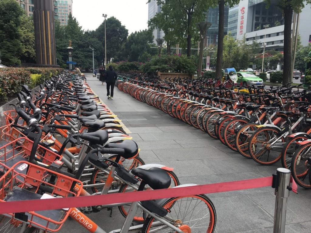 Bicycle deposits like this one are everywhere. Each ride has an electronic gizz which that lets you rent it using–what else?–WeChat. The system is not robustly communistlc: Different companies paint their bikes in different colors, and have sales to compete. Phredfoto. Click to enlarge